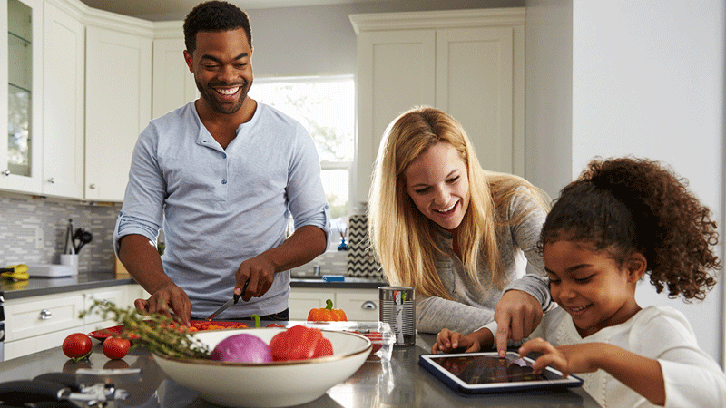 多样化的家庭在厨房用餐和使用平板电脑