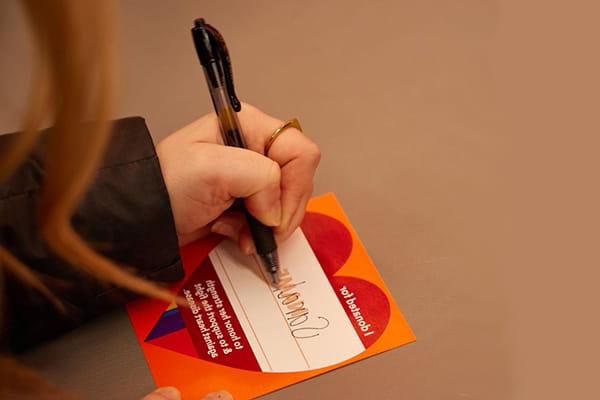 woman's hand writing a name on a heart-shaped donation paper
